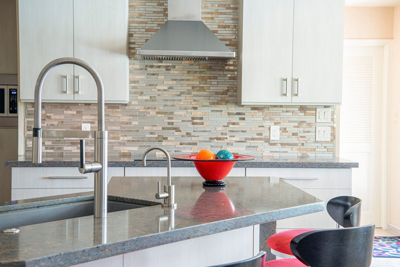 Contemporary kitchen interior with a sleek faucet and colorful fruit bowl on granite countertop.